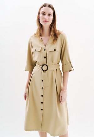 Robe khaki à boutons sur le devant, à manches courtes, avec deux poches poitrine, une ceinture à la taille avec une boucle ronde et une silhouette ample et fluide.