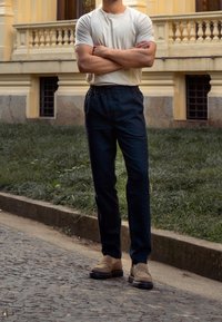 Ljusgrå kortärmad skjorta, mörkblå byxor med elastisk midja och beige loafers, mot en grönskande utomhusbakgrund.