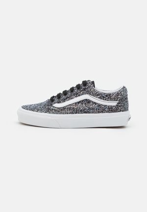Zapatilla baja con tela texturizada en blanco y negro, raya lateral blanca, cordones negros y suela de goma blanca sobre fondo liso.