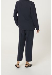 Granatowa marynarka i spodnie, dopasowane, z ustrukturyzowanym fasonem, gładką teksturą i minimalnym wyposażeniem, w zestawie z czarnymi sandałami na obcasie.