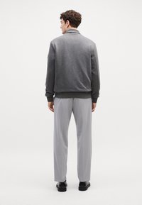 Felpa grigia con colletto e polsini a costine, abbinata a pantaloni di un grigio chiaro. Il tessuto sembra liscio con un design a vestibilità moderna.