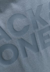 Gros plan sur un tissu texturé avec de grandes lettres en relief dans une couleur bleue mate assortie.