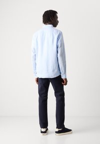Lichtblauw overhemdd met een zachte textuur, vergezeld van donkerblauwe broeken en marineblauwe sneakers met crèmekleurige accenten.