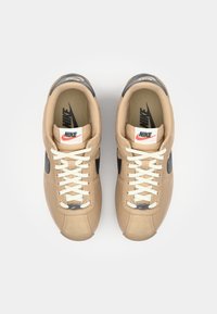 Rudi Nike sportbačiai su juodais akcentais. Su raišteliais, lygiu paviršiumi ir Nike logotipu ant liežuvėlio bei pado. Klasikinis stilius.