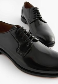 Chaussures noires en cuir avec une finition brillante, bout arrondi, design à lacets et détails de couture subtils. Texture lisse et profil élégant.