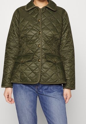 Veste matelassée vert olive avec boutons pression, poches à rabat et col arrondi portée sur un jean bleu.