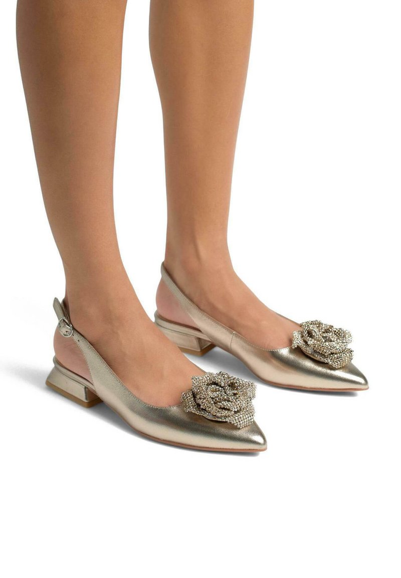Ballerines dorées métalliques à dos ouvert avec un bout pointu, ornées d'un accent de rose perlé. Talon bas et texture lisse.