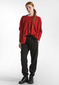 Maglione rosso over-size abbinato a pantaloni jogger neri e sneakers nere. Il maglione ha una vestibilità ampia; i pantaloni presentano una vita elastica.