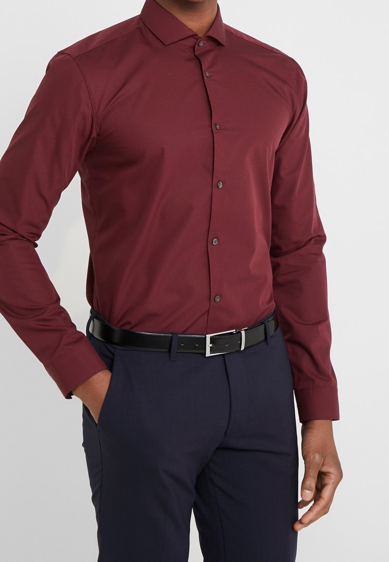 Bordeaux langemouwen overhemd met een button-down kraag en donkere knopen, gecombineerd met donkere broek en een zwarte riem met zilveren gesp.
