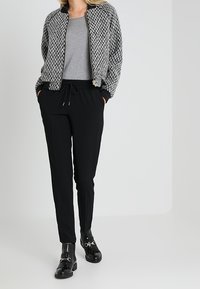 Šedý a černý houndstooth bomber kabát přes šedý top, kombinovaný s černými zúženými kalhotami a černými kotníkovými botami s přezkovými detaily.