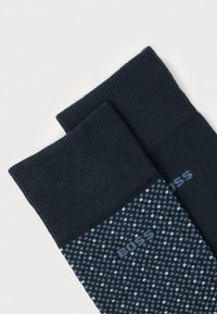 Δύο διπλωμένες σκούρες μπλε κάλτσες φορέματος με μικρές ανοιχτό μπλε και λευκές κουκκίδες και το λογότυπο "BOSS" σε λευκό φόντο.