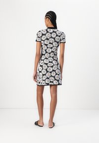 Svart blomstret kjole med hvite prekestoler og gule midtpunkt. Korte ermer, tettsittende design, og kne-lengde kant. Brukt med svarte glidesandaler.