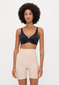 Mustmustritud must rinnahoidja laineliste äärtega, valmistatud siledast kangast, koos kõrge talje ja naha värvi vormivatel lühikestel, mõlemad minimaalistlikus disainis.