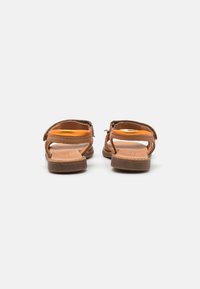 Bruine leren sandalen met een platte zool, open teen en verstelbare banden, met een gladde textuur en minimale stikdetails.