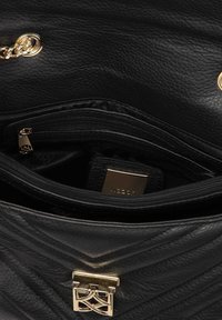 Borsa a tracolla nera in pelle con texture trapuntata, hardware dorato e chiusura con zip. L'interno presenta una tasca con zip aggiuntiva e il logo del marchio.