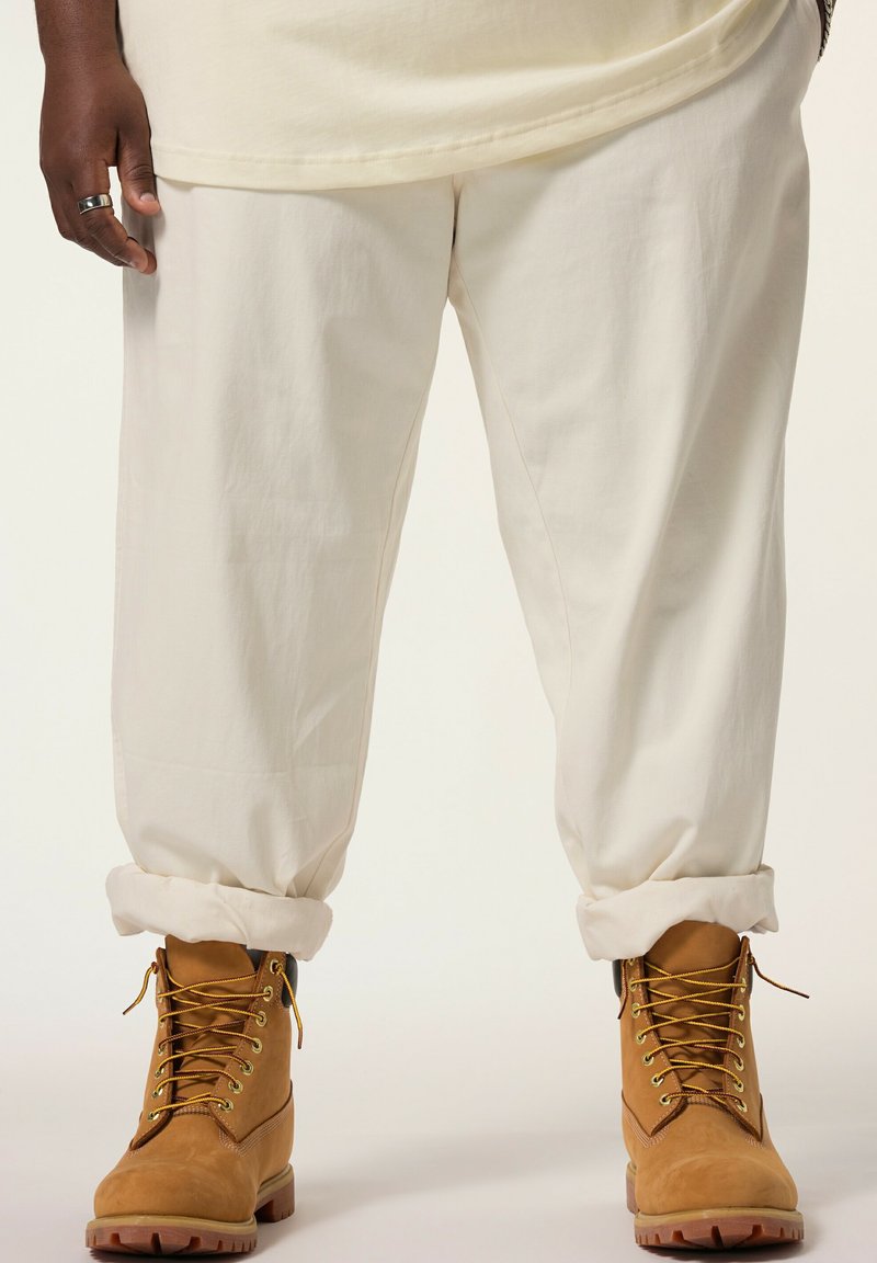Stivali da lavoro beige con lacci, occhielli dorati e suole in gomma spessa, abbinati a pantaloni beige arrotolati ai polsini.
