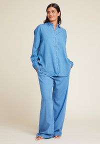 Lys blå denimskjorte kombinert med løstsittende lys blå bukser. Begge har en avslappet design, knappestolpe foran og lange ermer.