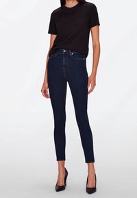 Camiseta de algodón negra combinada con jeans ajustados de color azul oscuro. Los jeans tienen una cintura alta y un corte slim, con costuras sutiles y bolsillos.