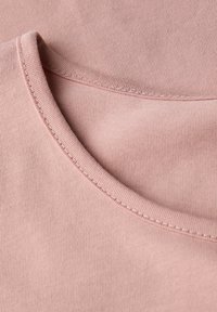 Gros plan sur un tissu en coton rose doux à col rond, avec des coutures fines visibles le long de la couture du col.