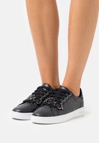 Baskets en cuir noir avec finition texturée, semelle blanche et accents métalliques au niveau des lacets. Présentent un détail de logo rond.