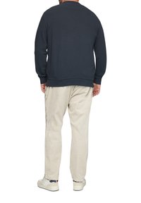 Granatowy sweter z długimi rękawami i ściągaczami, w połączeniu z jasnobeżowymi spodniami z sztruksu i białymi sneakerami. Z pokazanym widokiem z tyłu.