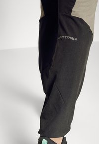 Svarta och grå idrottsbyxor med en texturerad finish, med snedställda sömmar och "KARI TRAA"-logotypen i vitt på låret.