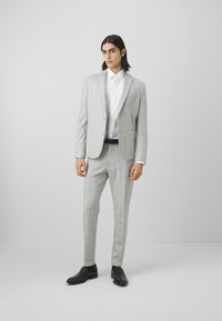 Ljusgrå kostym med texturerad yta, bestående av en enfärgad blazer, vit skjorta med krage, slim fit byxor och svarta läderskor.