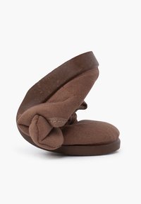 Chausson en tissu brun avec un design noué sur le dessus, semelle en mousse et un talon arrondi légèrement surélevé. Texture douce.