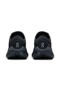 Baskets de sport noires avec une tige texturée, un talon arrondi et un logo proéminent à l'arrière. Elles disposent d'une semelle épaisse et solide avec une bonne traction.