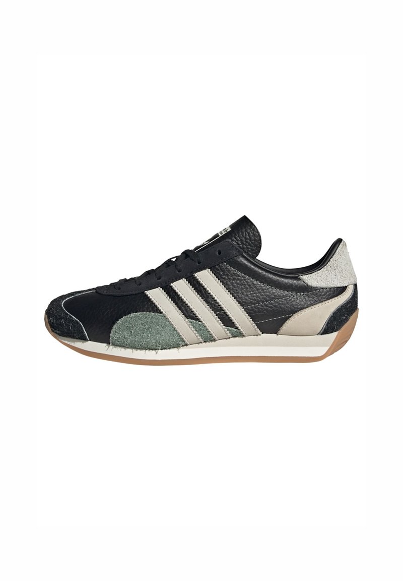 Black and green suede sneaker with textured leather, three white stripes, a rubber sole, and a rounded toe. Features intricate stitching.