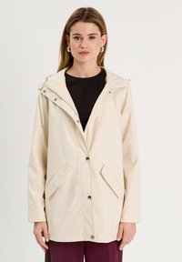 Veste beige, résistante à l'eau, avec capuche, dotée d'une fermeture à boutons, de poches latérales et d'une texture lisse. Design simple avec des accents minimaux.