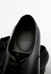 Chaussures habillées en cuir noir avec lacets, montrant l'intérieur de la chaussure droite avec la marque "Massimo Dutti" sur la semelle intérieure.