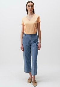 T-shirt a V in pescozzo abbinata a jeans a gamba larga blu chiaro e scarpe slip-on beige. Design semplice e minimalista.