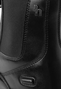 Bota de cuero negra con un panel texturizado, costuras discretas y un acento de logo metálico. Acabado suave con un diseño de punta redondeada.