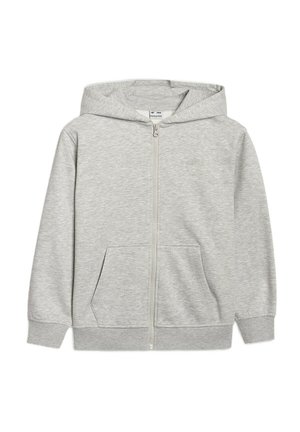 Dziecko stoi, ubrany w szarą bluzę rozpinaną, pasujące spodnie dresowe, ciemną koszulkę i szare sneakersy na jednolitym tle.