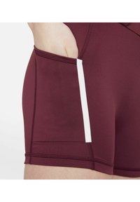 Donkerrode sportbroek met een witte zijstreep en een zak aan de linkerzijde. De stof is glad met zichtbare stikseldetails.