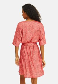 Květinové šaty v korálové barvě, s krátkými rukávy, volným střihem a látkovým páskem v pase pro nastavitelnou velikost.