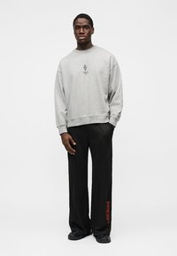 Gray sweatshirt with a round neckline and logo at the center, paired with black trousers featuring red text along the side.