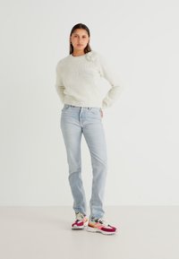 Off-white pleteno pulover z rebrastim robom in cvetličnim poudarjanjem, kombiniran z svetlo modrimi jeans hlačami in večbarvnimi športnimi čevlji.