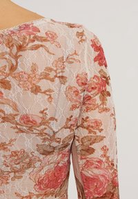 Top in pizzo con un motivo floreale nelle tonalità di rosa e marrone, caratterizzato da una delicata texture trasparente e scollo rotondo.