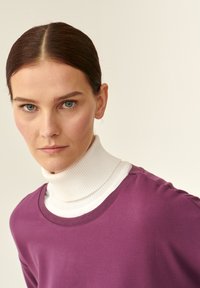 Ljubičasta majica dugih rukava s okruglim izrezom složena preko bijelog rebrastog turtleneck-a. Glatka tkanina s lagano prilagođenim siluetom.