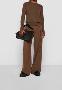 Pull en tricot marron, pantalon large marron avec plis, et un sac en cuir noir. La tenue présente une coupe décontractée et des textures lisses.