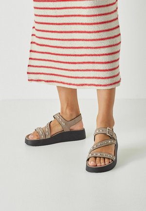 Grå sandaletter med metaløjer, en tekstureret sort kilehæl og justerbare ankelstropper, kombineret med en stribet stofkjole.