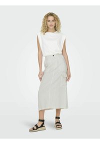 Top sin mangas blanco combinado con una falda larga a rayas en tonos beige y crema, con un bolsillo lateral y un detalle de botón. Sandalias de plataforma negras.