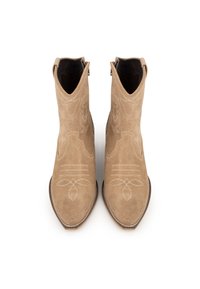 Botas de vaquero de ante beige con puntas afiladas, patrones de costura decorativa y bucles de agarre. Suelas planas y acentos de hardware mínimos.