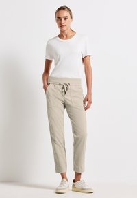 Pantalons beige clair avec une taille élastiquée, poches latérales et chevilles effilées, associés à un T-shirt blanc ajusté et des baskets blanches.