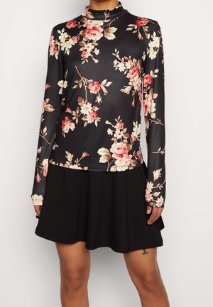 Black long-sleeve turtleneck top with pink and white floral pattern paired with a black flared skirt worn by a person.