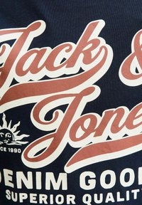 T-shirt navy con testo audace in bianco e rosso che recita "Jack & Jones" e "Denim Good" accompagnato da una grafica del sole. Tessuto in cotone con una finitura liscia.