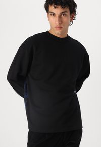 Hanorac negru cu mâneci lungi, guler rotund și accente texturate de culoare albastră pe laterale. Material moale, croială lejeră, design minimalist.