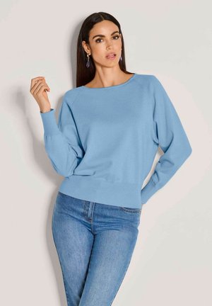 Lichtblauwe gebreide trui met een brede halslijn, verlaagde schouders en geribbelde zoom. Gepaard met strakke blauwe jeans.
